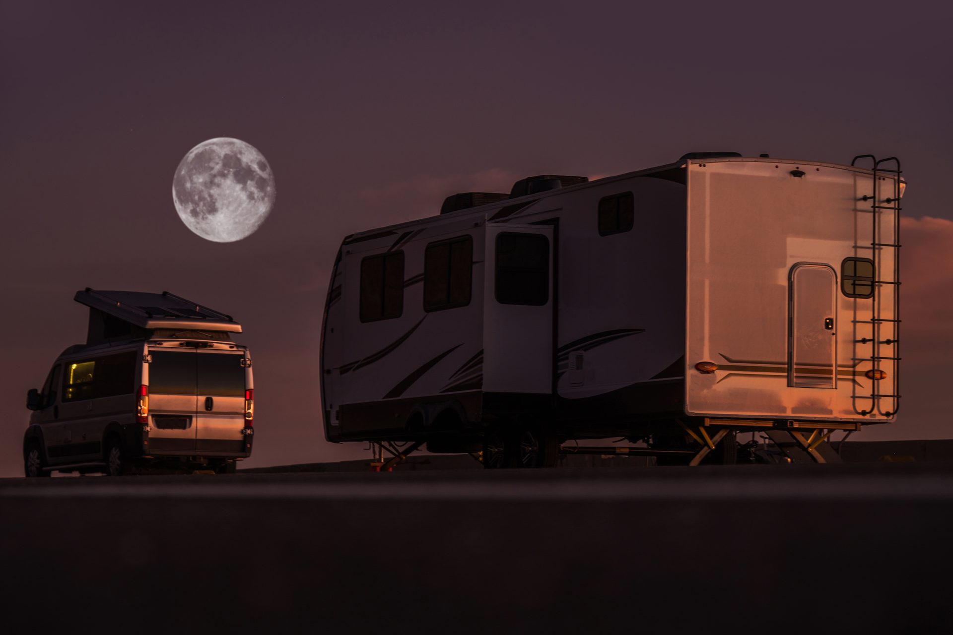 RVs parked under a full moon at a desert campground at night