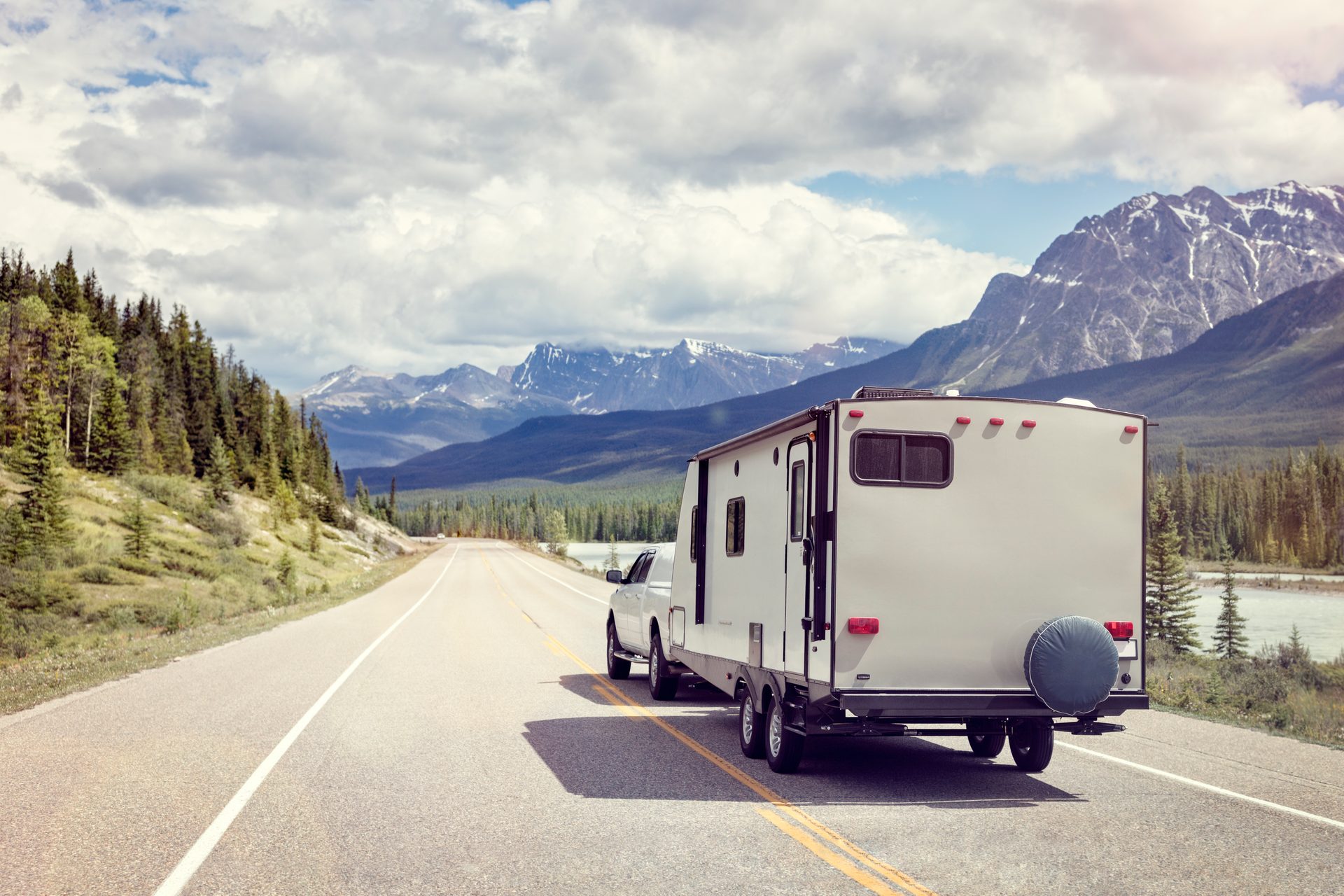 Travel trailer being towed along a scenic mountain highway with dramatic peaks in the background
